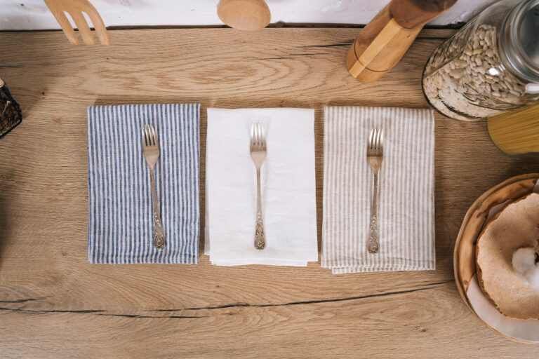 Top view of dining utensils arranged on striped kitchen towels on a wooden surface.